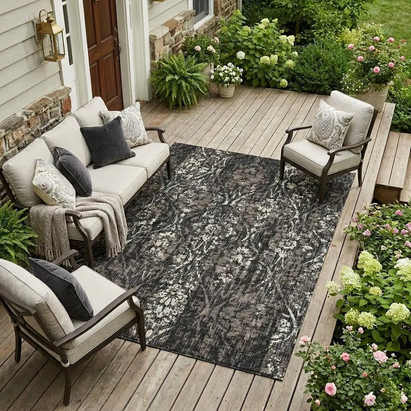 Gray floral outdoor rug on wooden deck, surrounded by plush seating and lush greenery, perfect for patio decor.