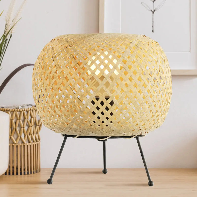 Woven bamboo table lamp with a gold finish, featuring a round shape and black metal legs for a stylish accent.