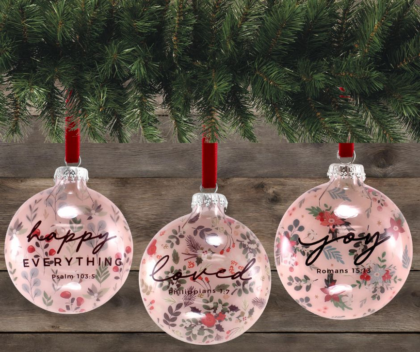Set of three round pink Christmas ornaments with red hanging ribbons and floral text