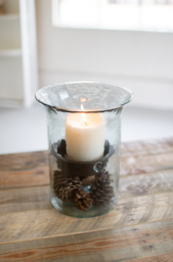Glass candle cylinder with glowing white candle and pinecone-filled rustic insert