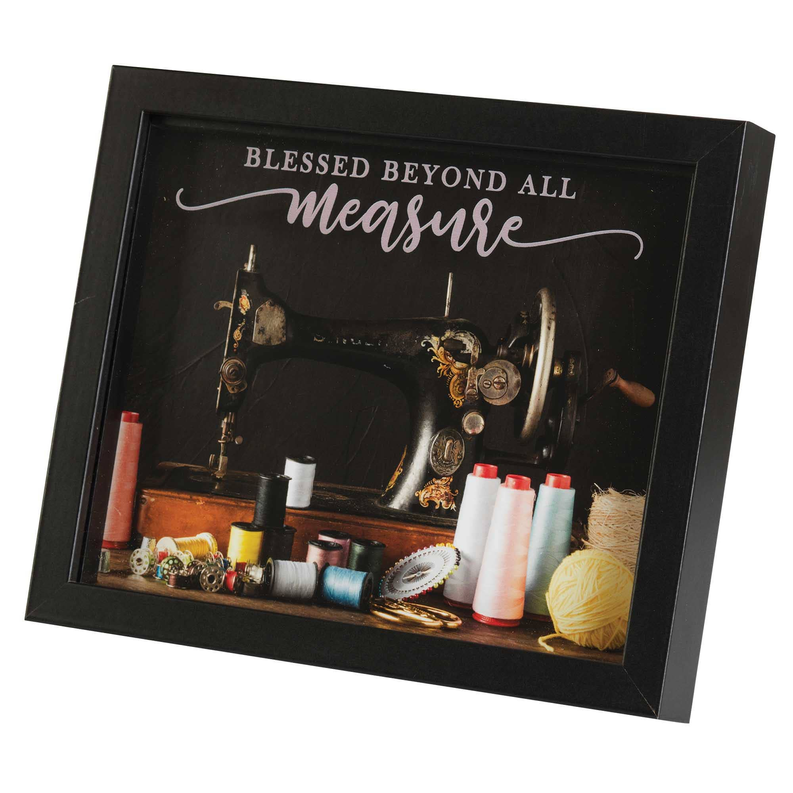 Tilted framed sewing wall art with “Blessed Beyond All Measure” and fabric rolls