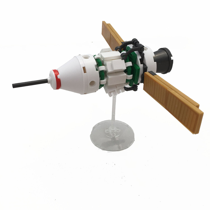Spacecraft building brick kit model: white capsule, green blocks, black engine, on stand