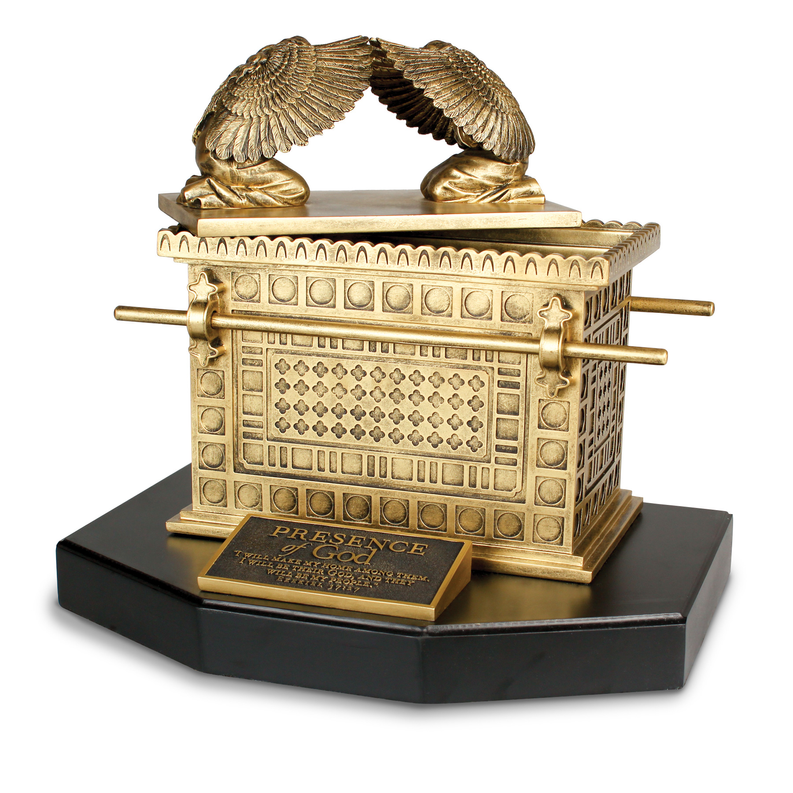 Golden religious sculpture with ark shape, winged figures, and cross on a black base