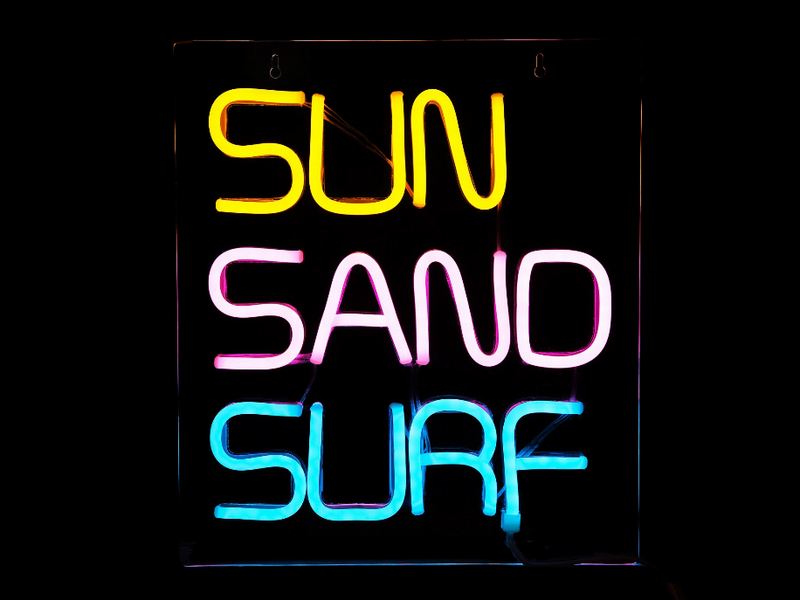 LED neon sign displaying "SUN SAND SURF" with yellow, pink, and blue glowing letters