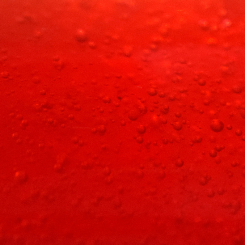Red wax surface close-up with glossy sheen and small droplets