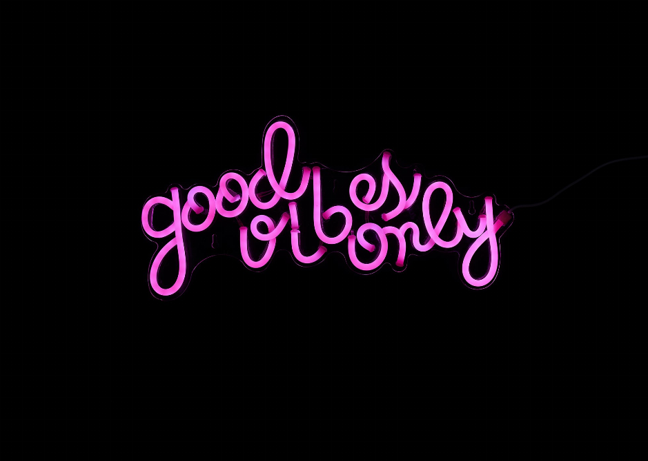 Pink illuminated cursive “Good Vibes Only” LED neon sign, centered.