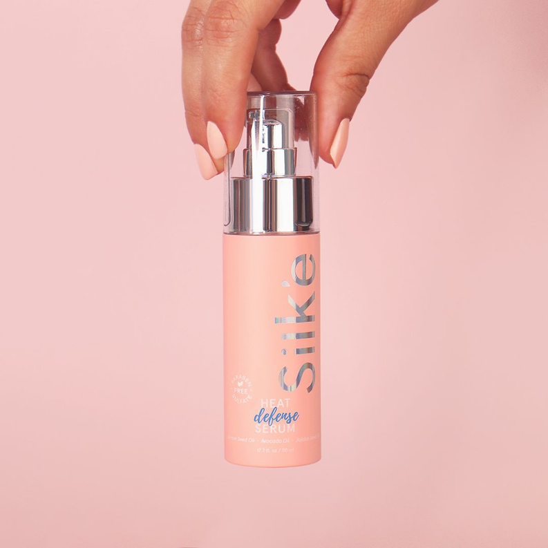 Silk'e Heat Defense Serum bottle held by hand, showing silver pump and pink glass