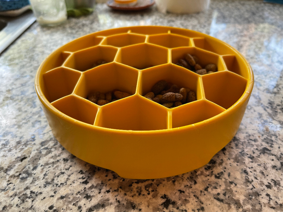 Yellow honeycomb slow feeder bowl on countertop with kibble in raised hex compartments
