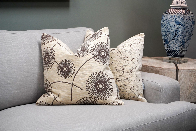 Cream throw pillows with black circular dotted rosette line pattern on a light sofa.