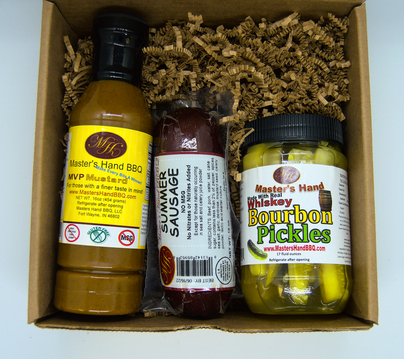 Open kraft gift set with three bottles, shredded paper filler, BBQ sauce and pickles.