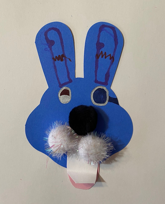 Blue bunny cut-out with black nose, drawn eyes, and fluffy white pom-poms