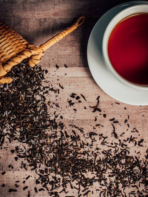 Pile of dark dried lavender herb leaves beside a cup of red tea