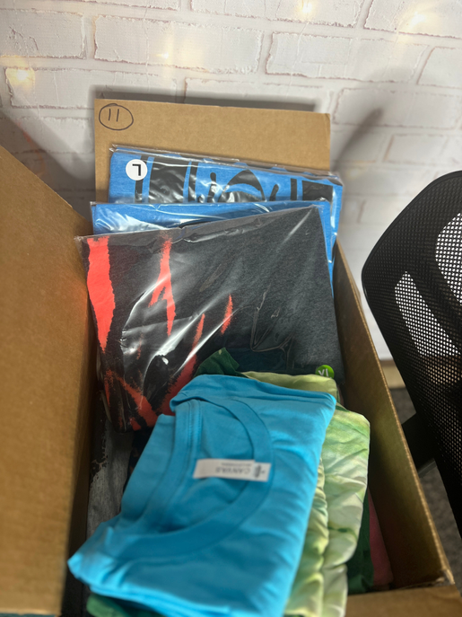 Mystery box with folded shirts in blue, black, red, and green inside an open cardboard case