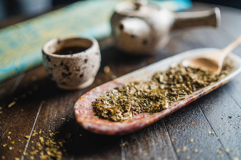 Ceramic mate cup and wooden spoon filled with green yerba herbs