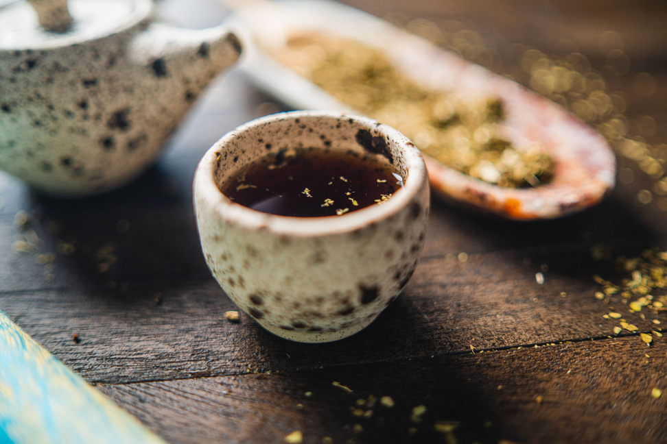 Speckled ceramic mate cup with dark tea and scattered green herbs