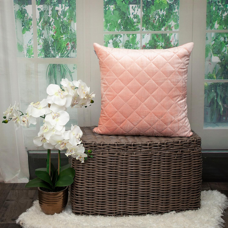 Blush pink square throw pillow with diamond quilting on wicker chair
