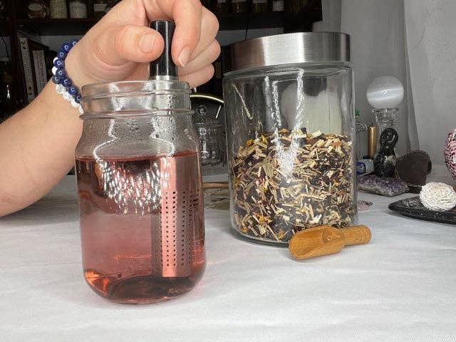 Tea stick infuser held over glass mug; perforated stainless-steel tube for loose leaf tea