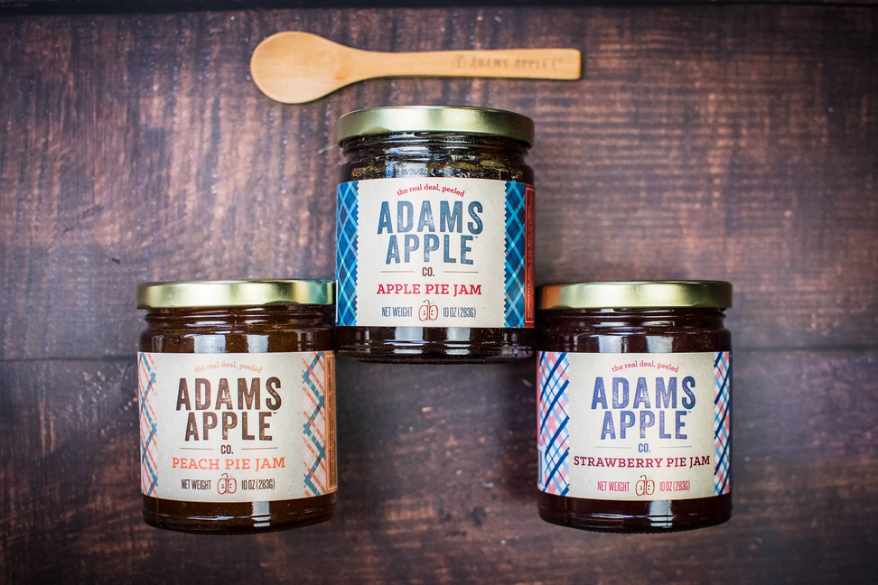 Three ADAMS APPLE preserves jars stacked, with wooden spoon on top
