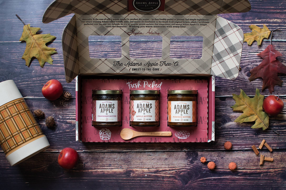 Open gift box holding three ADAMS APPLE jars, with autumn leaves around