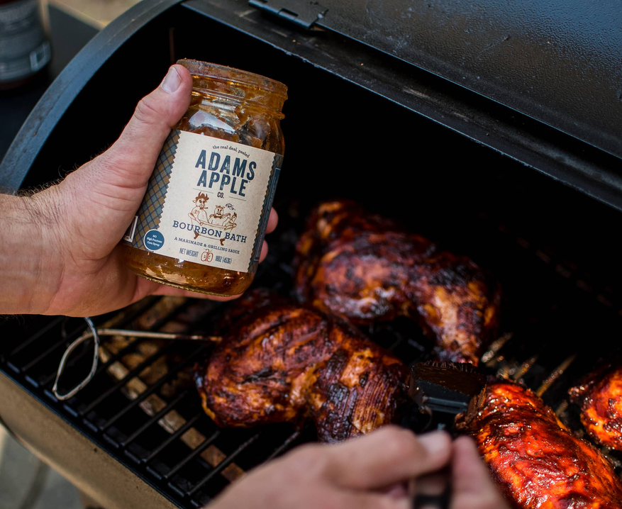 Bourbon bath BBQ sauce bottle in hand beside grilled chicken