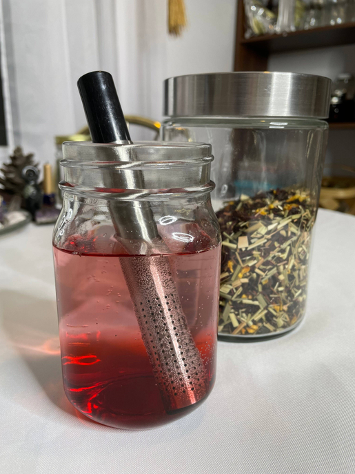 Tea stick infuser with perforated metal tube and black cap for loose leaf tea, in glass