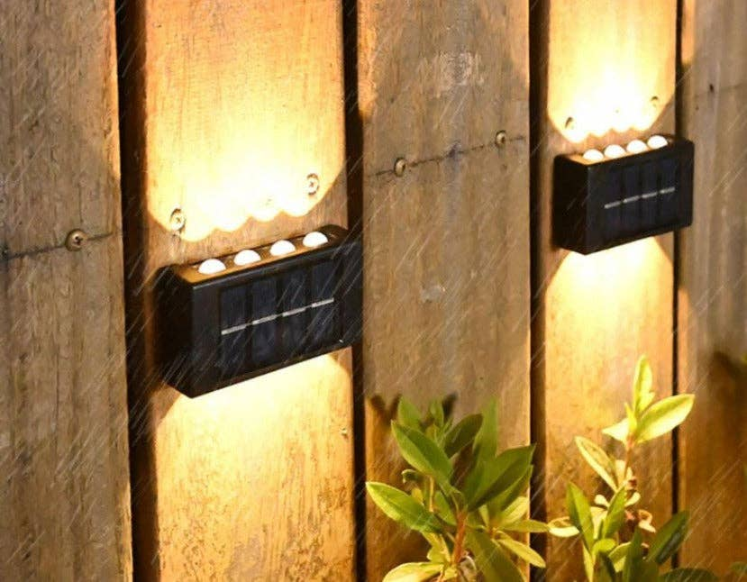 Two black solar wall LED lights mounted on wooden fence, warm glowing illumination