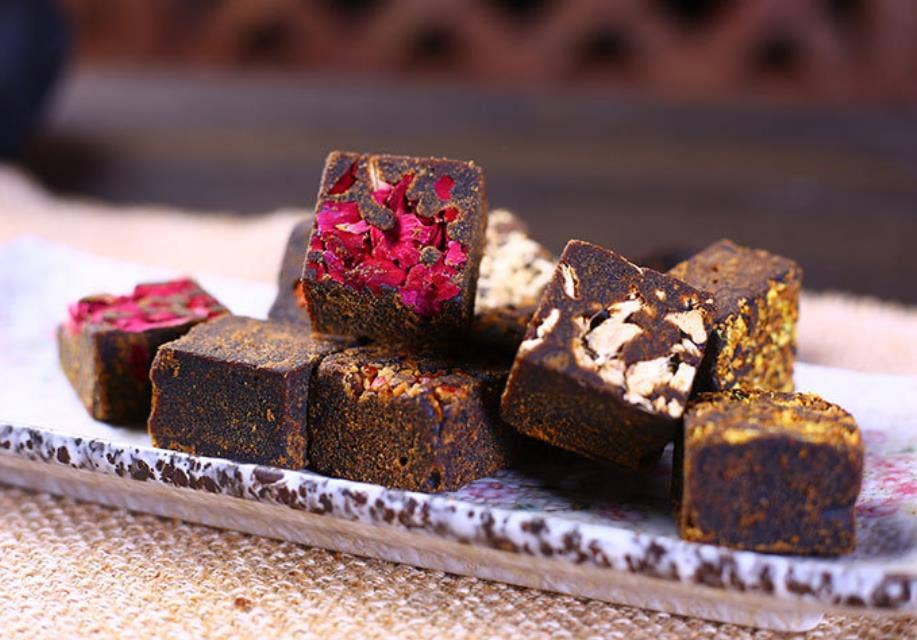 Brown sugar cubes with red dried fruit and flower bits on top, on a tray