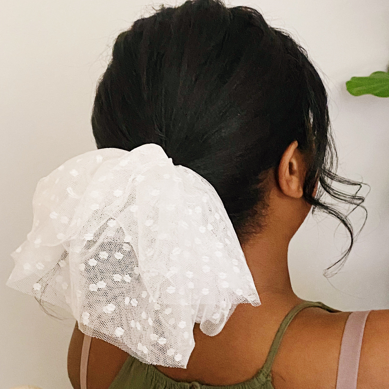 White tulle hair scrunch worn on dark hair, sheer dotted ruffle top