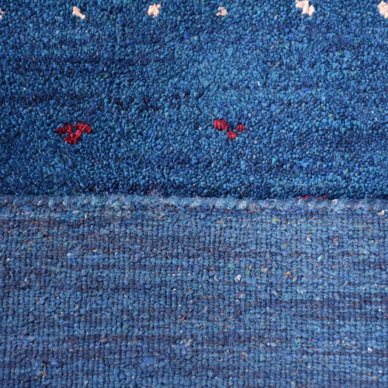 Blue rug detail with dense loop pile and sparse multicolor motif accents across surface