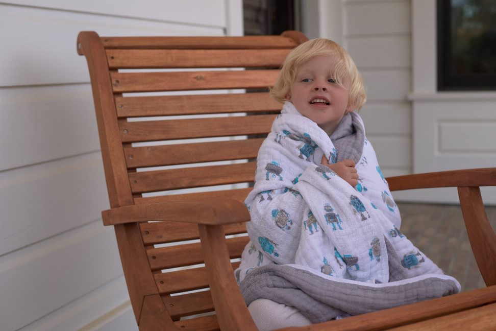 Robot-pattern baby blanket draped on a child, teal robot print on light fabric