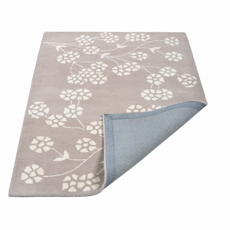 Taupe wool rug corner with white floral design and folded backing