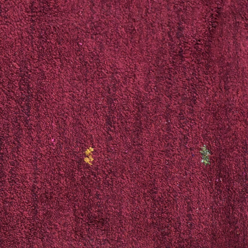 Maroon rug pile close-up with small yellow and green speckles