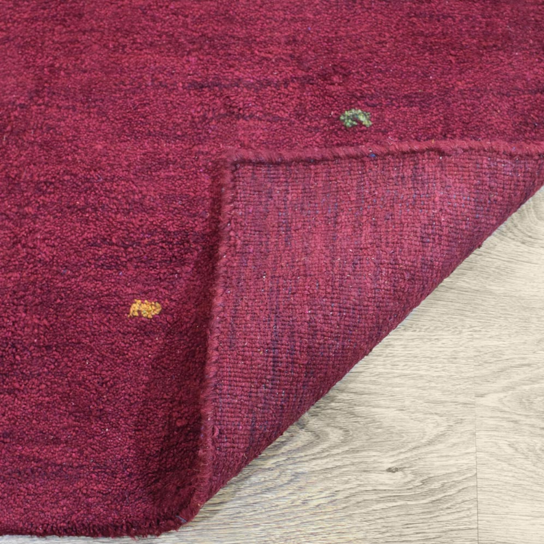 Maroon speckled area rug corner detail with short fringe and textured border
