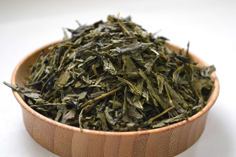 Panfired green tea leaves close-up in a wooden bowl, dark green dried tea