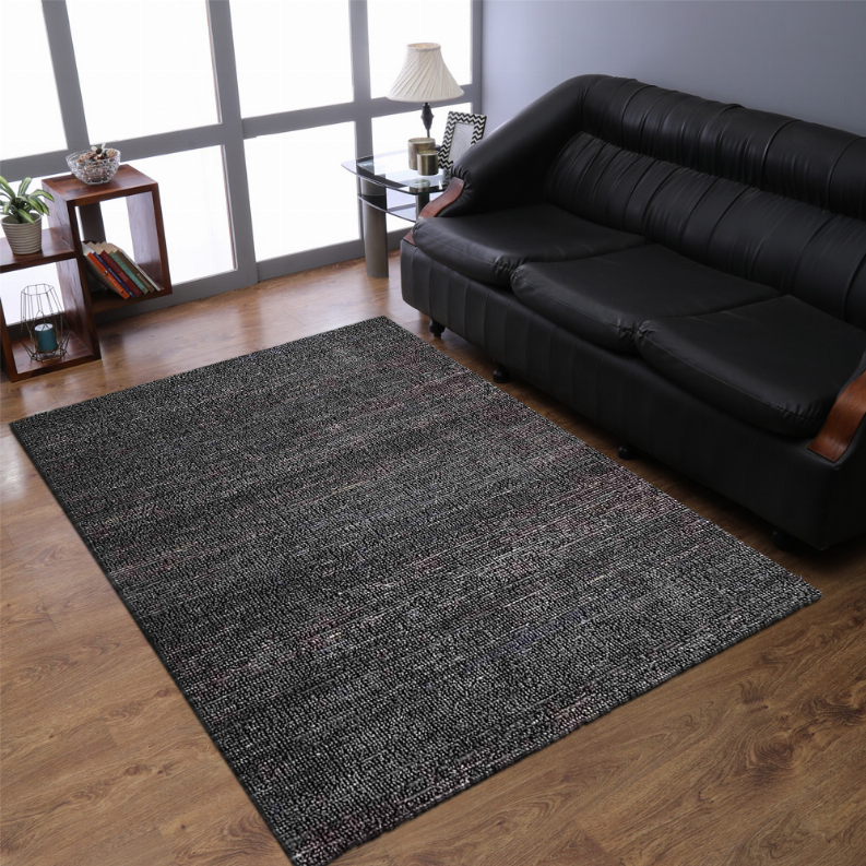 Charcoal hand-woven jute area rug in front of a black leather sofa