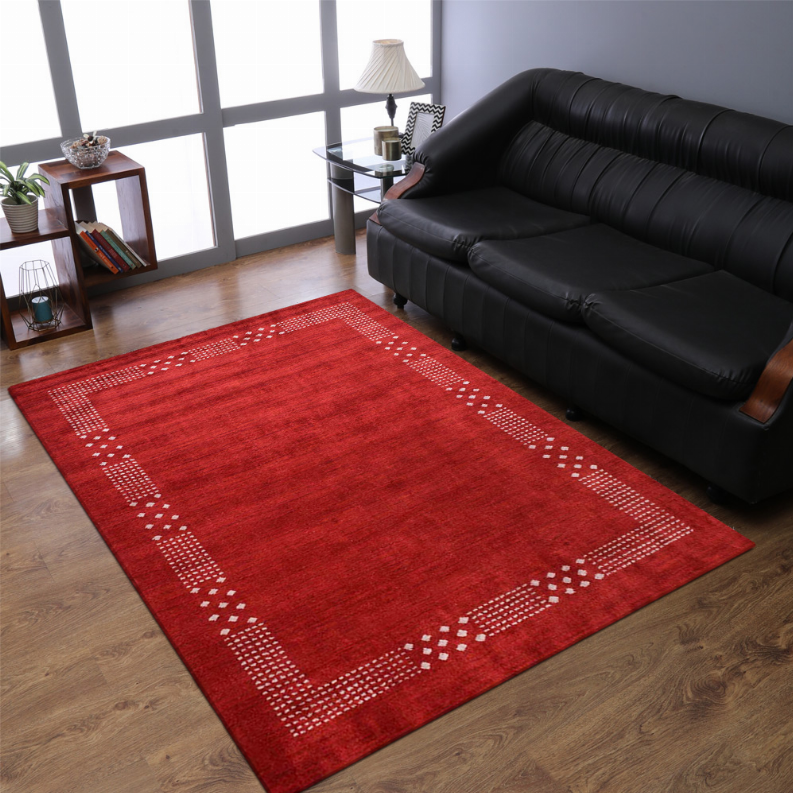 Red area rug with white geometric border on wood floor beside black sofa