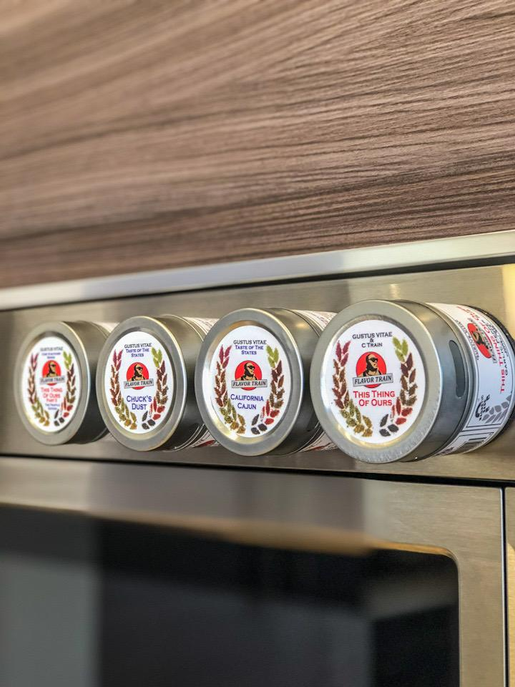 Set of four seasoning tins with round labels in a metal canister row