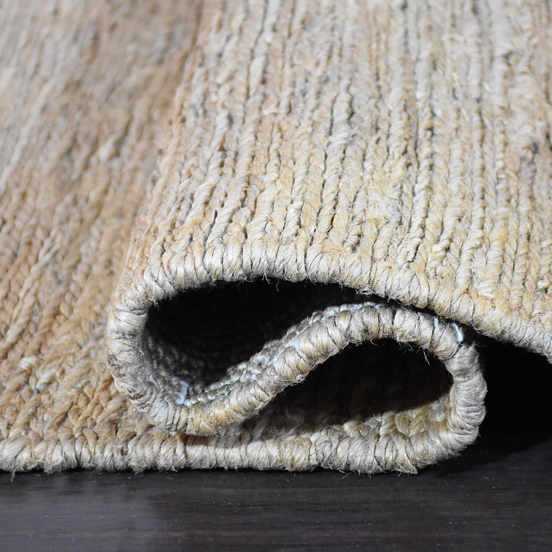 Rolled corner of solid light beige hand woven jute area rug showing underlayer