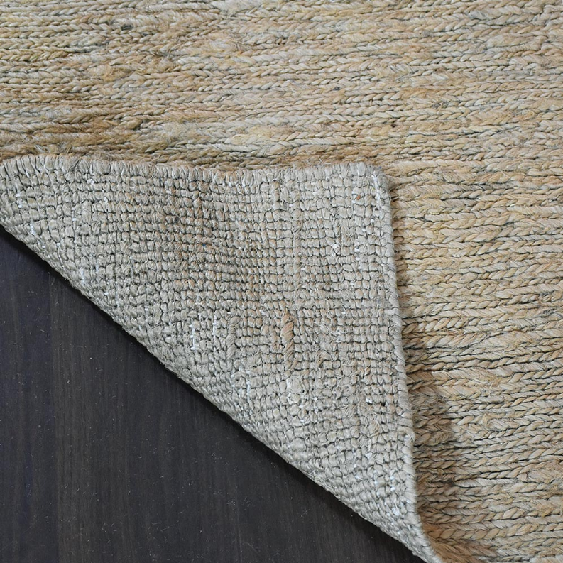 Close-up of jute area rug corner and backing in light beige on dark floor