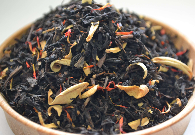 Loose dark tea leaves with pale peach slices in a wooden bowl, close-up
