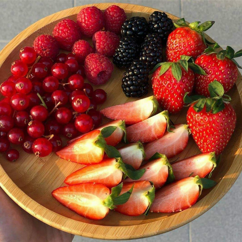 Round wooden serving plate filled with strawberries, blueberries, and blackberries