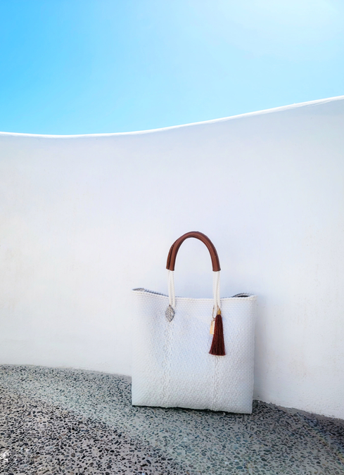 White woven tote bag with curved brown handles and hanging tassel charm
