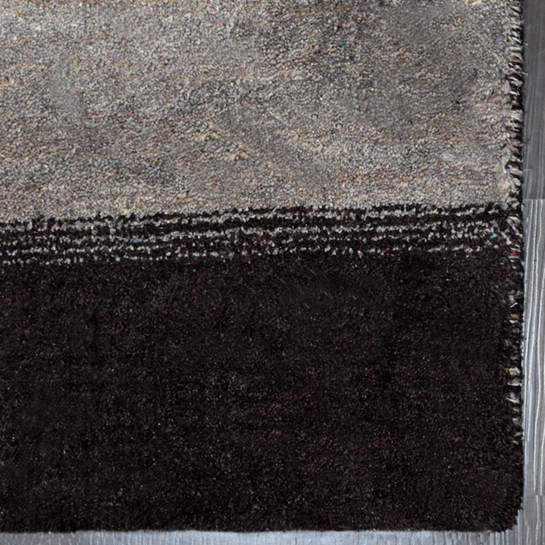 Hand-knotted area rug corner close-up with gray speckled top and dark charcoal body