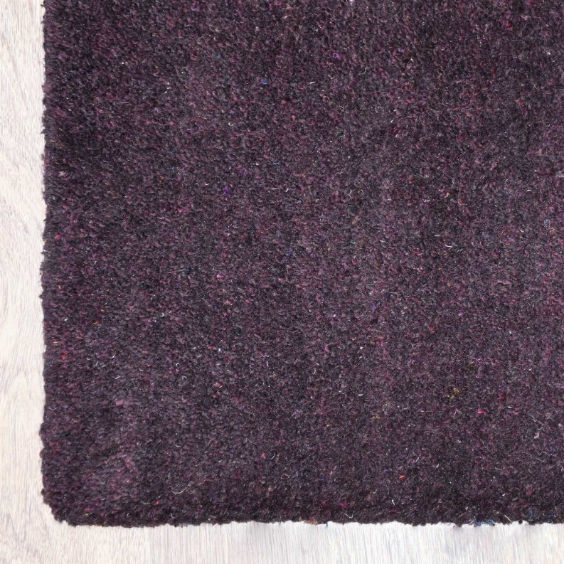 Dark purple hand-knotted rug surface close-up with textured, speckled pile