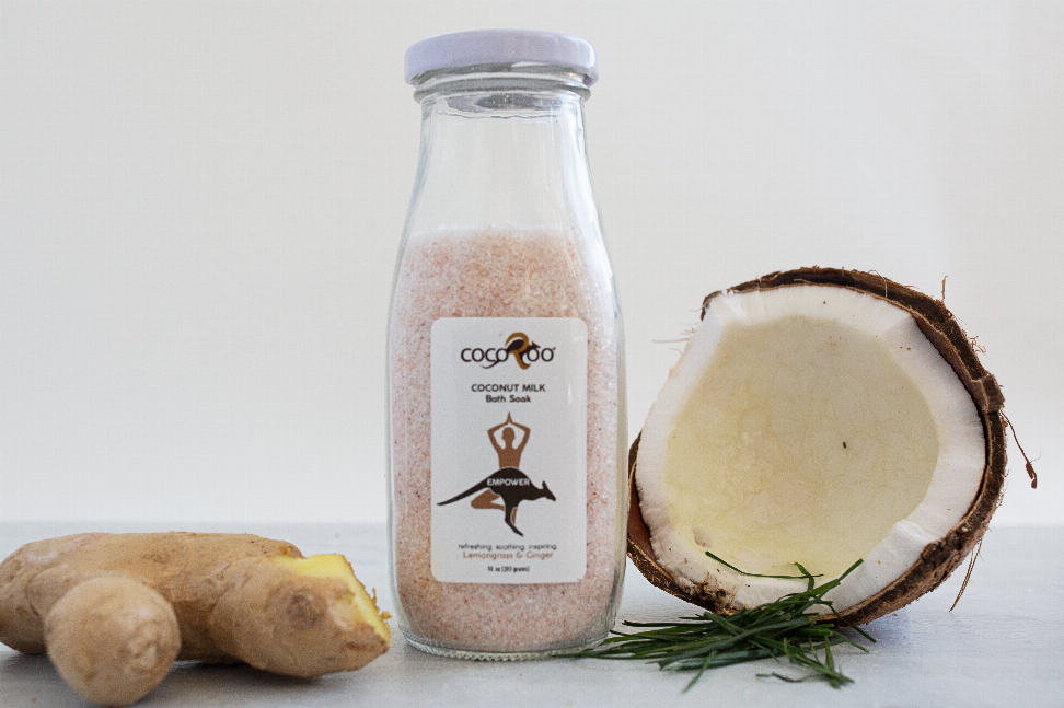 Coconut milk bath soak jar with label, beside coconut half and ginger root