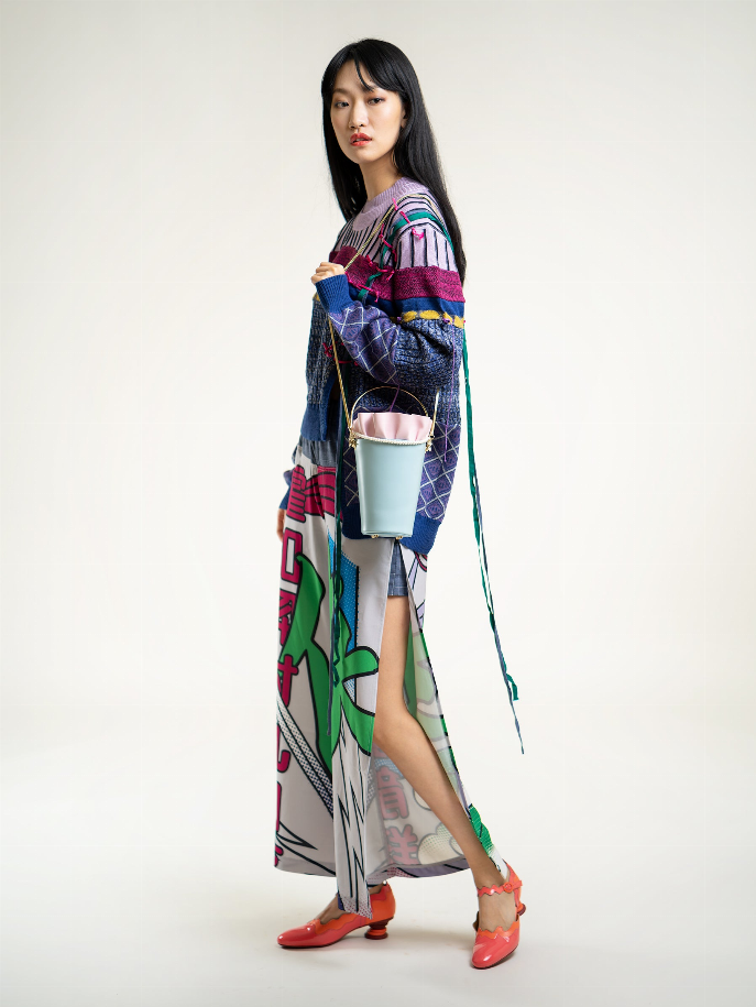Light blue bucket bag with pink ruffle top and gold chain strap, held at side