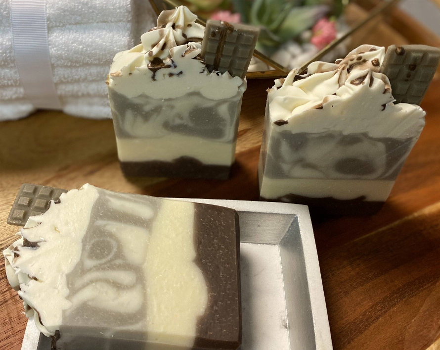 Soap bar close-up, creamy white base with chocolate-brown swirl and embedded chocolate square