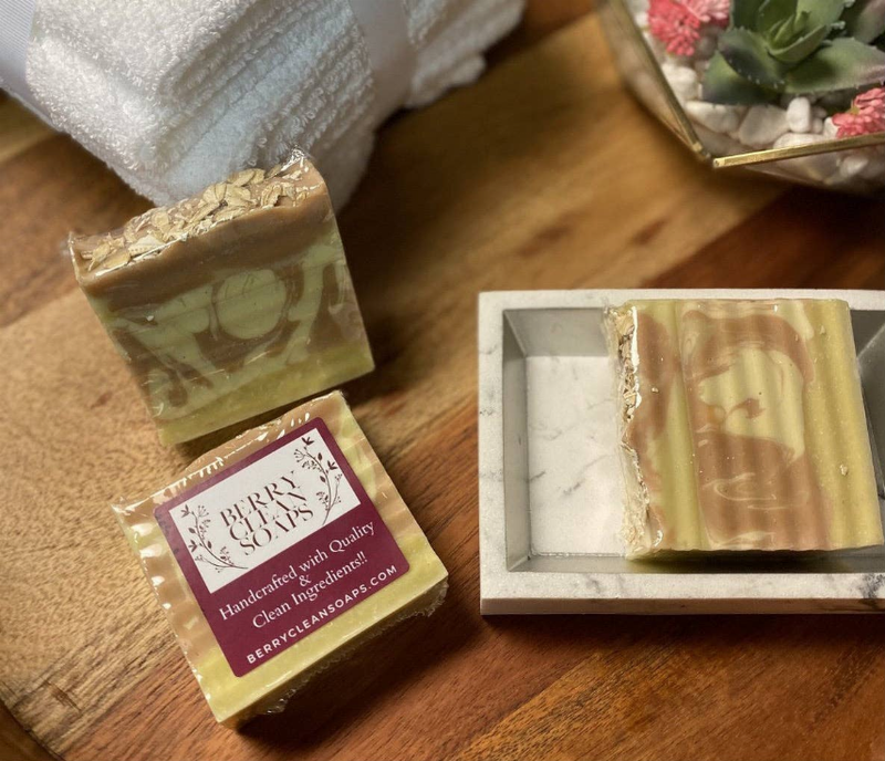 Almond oats soap bar wrapped in clear plastic, beside a bar in a gray tray