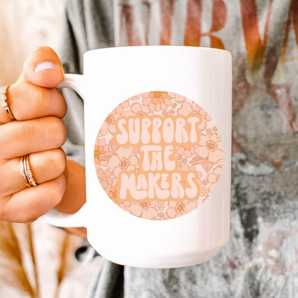 White ceramic 15oz coffee mug with floral 'Support the Maker's' print.