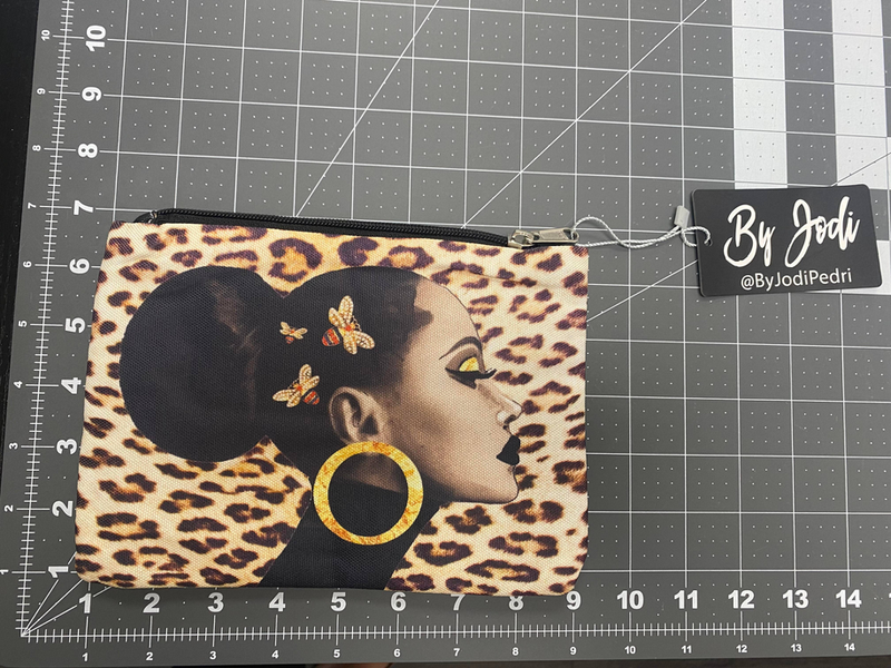 Leopard-print zipper pouch with wrist strap; graphic face and gold ring detail.